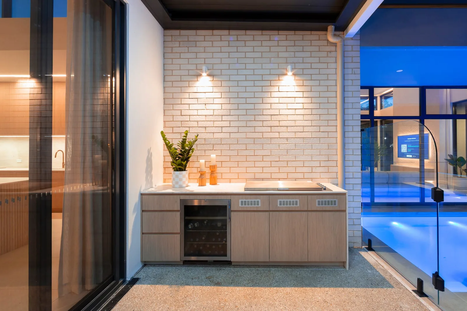 The outdoor kitchen at dusk, a built-in barbecue and bar beside the pool