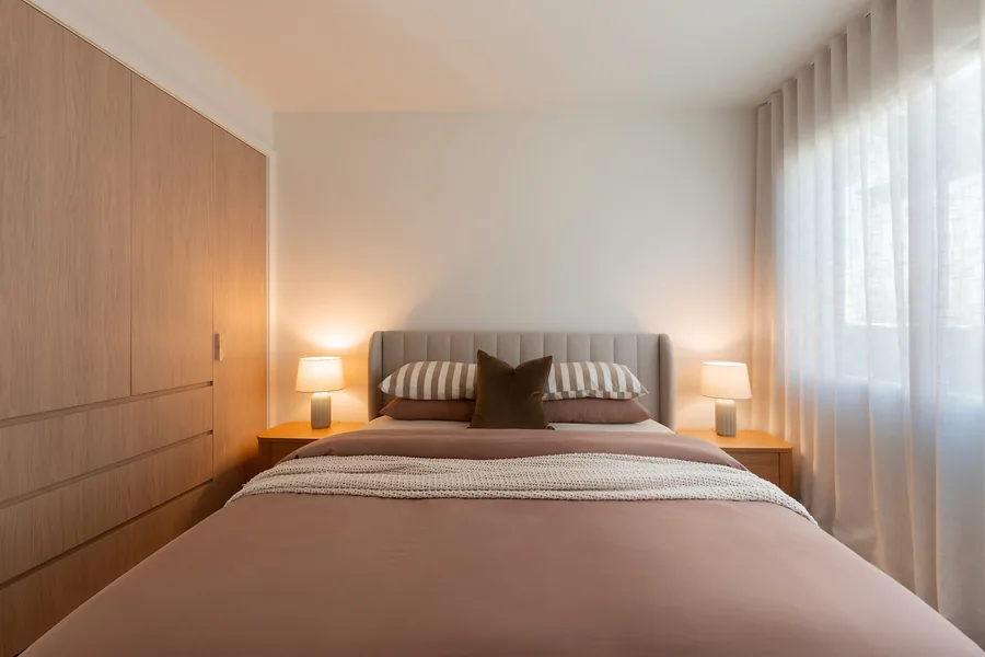 A bedroom, the bed against warm timber with a lamp either side