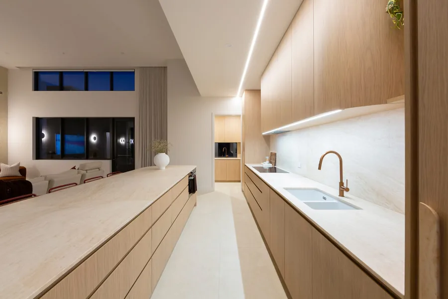 The kitchen at dusk, stone benches and brushed copper tapware under high windows