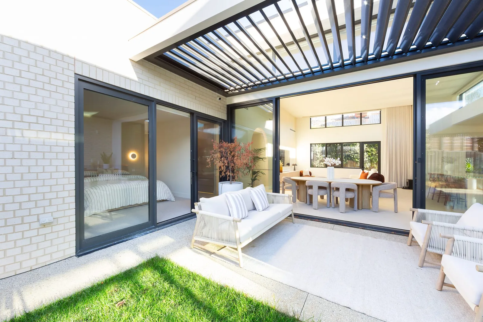 The courtyard under a louvred roof, outdoor seating on the lawn outside the glass (the tour that opens is of another home)